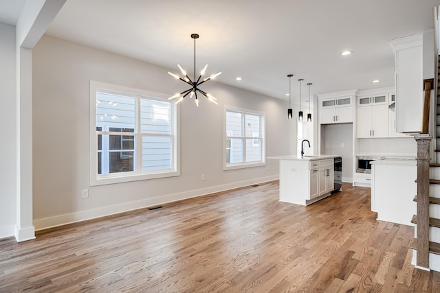 kitchen featuring light wood finished floors, tasteful backsplash, wine cooler, a sink, and a notable chandelier