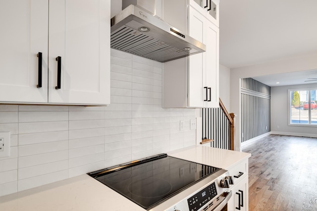 kitchen with wall chimney exhaust hood, stove, and white cabinetry