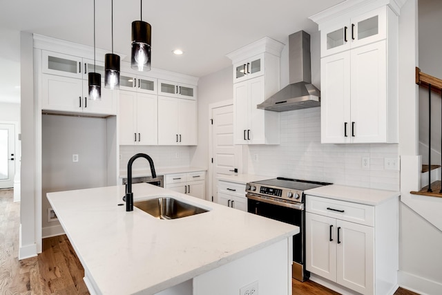 kitchen with a center island with sink, stainless steel electric range oven, light countertops, wall chimney range hood, and a sink