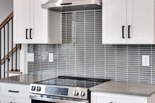 kitchen featuring tasteful backsplash, white cabinetry, dark stone counters, under cabinet range hood, and stainless steel electric range