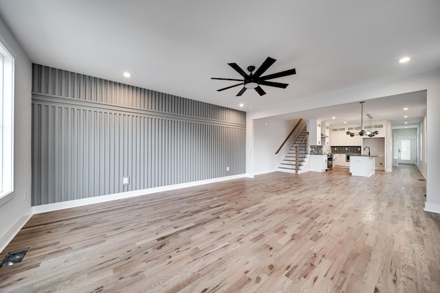 unfurnished living room featuring light wood-type flooring, a sink, recessed lighting, and stairs