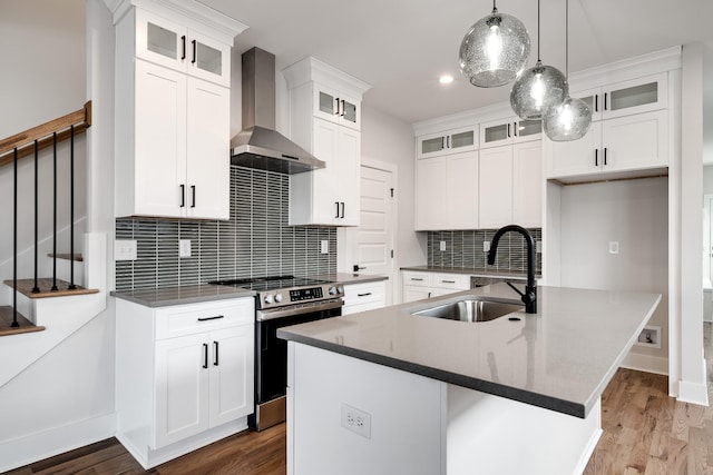 kitchen with wood finished floors, a sink, stainless steel range with electric cooktop, wall chimney range hood, and dark countertops