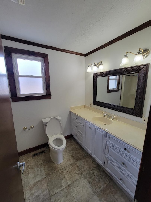 bathroom featuring toilet, vanity, baseboards, visible vents, and crown molding