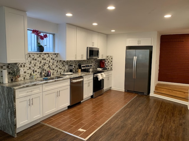 kitchen featuring light stone counters, dark wood-type flooring, stainless steel appliances, white cabinetry, and a sink