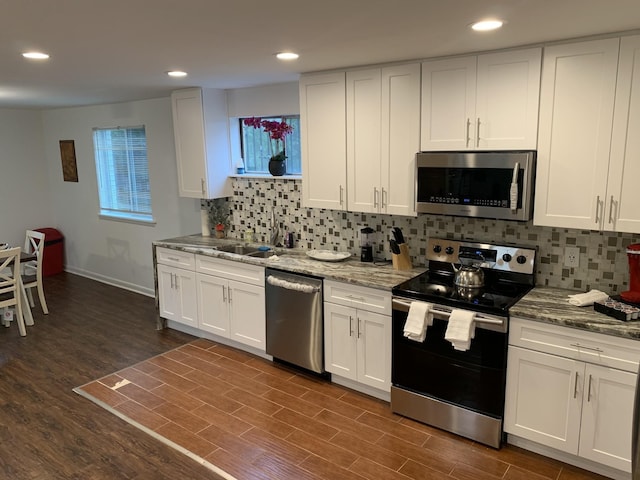 kitchen featuring light stone counters, dark wood-style floors, appliances with stainless steel finishes, white cabinets, and a sink