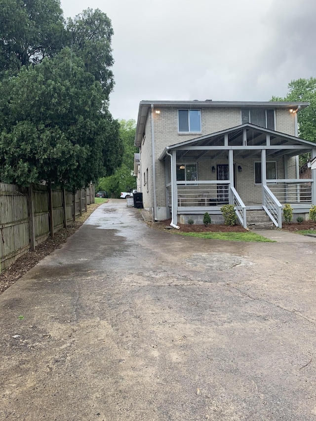 view of front of property with covered porch, driveway, brick siding, and fence