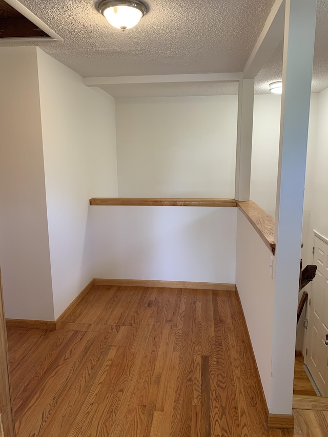 interior space featuring a textured ceiling, light wood finished floors, and baseboards