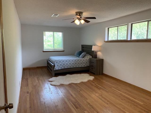 bedroom with baseboards, visible vents, ceiling fan, a textured ceiling, and light wood-style floors