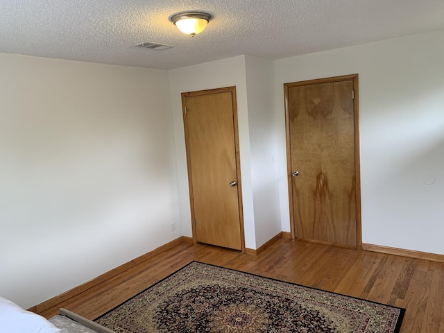 bedroom featuring visible vents, a textured ceiling, baseboards, and wood finished floors