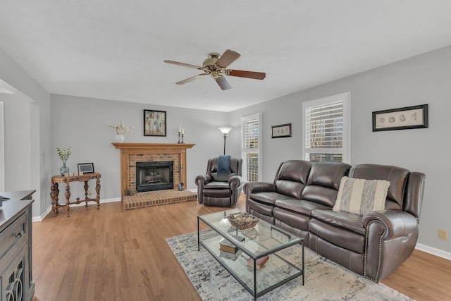 living room featuring ceiling fan, a fireplace, light wood-style flooring, and baseboards