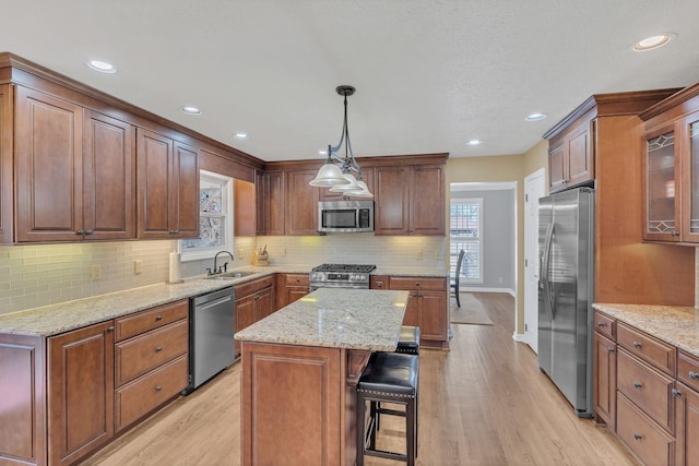 kitchen featuring glass insert cabinets, stainless steel appliances, a sink, a center island, and decorative light fixtures