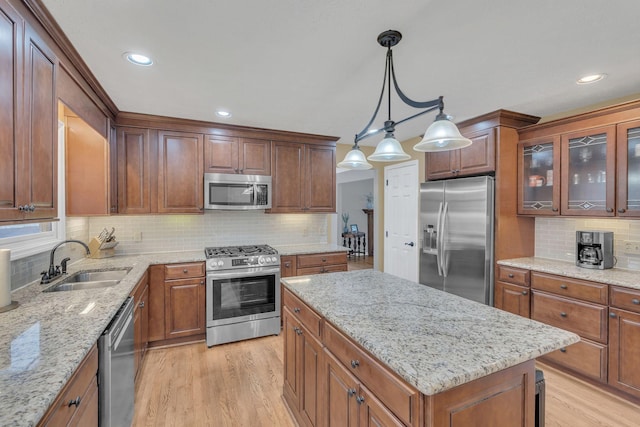 kitchen featuring decorative light fixtures, appliances with stainless steel finishes, glass insert cabinets, a kitchen island, and a sink