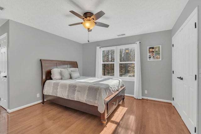 bedroom featuring light wood-type flooring, baseboards, visible vents, and a textured ceiling