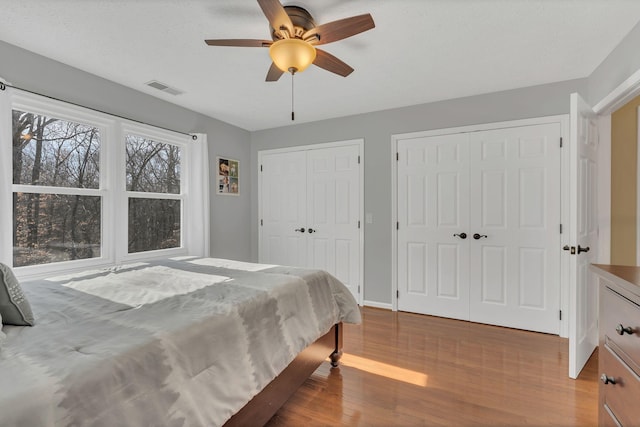 bedroom with baseboards, visible vents, ceiling fan, wood finished floors, and multiple closets