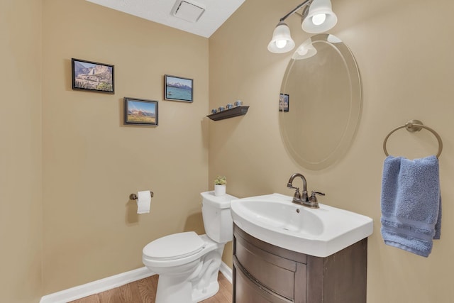 half bathroom featuring wood finished floors, vanity, toilet, and baseboards