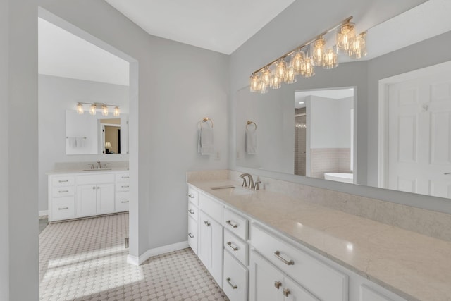 full bath featuring a stall shower, two vanities, a sink, and baseboards