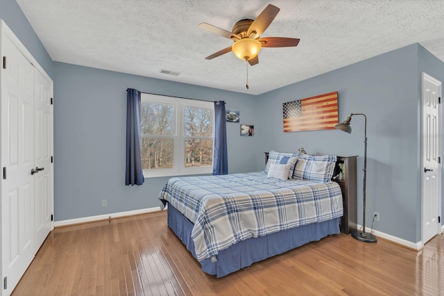 bedroom featuring visible vents, a ceiling fan, a textured ceiling, wood finished floors, and baseboards