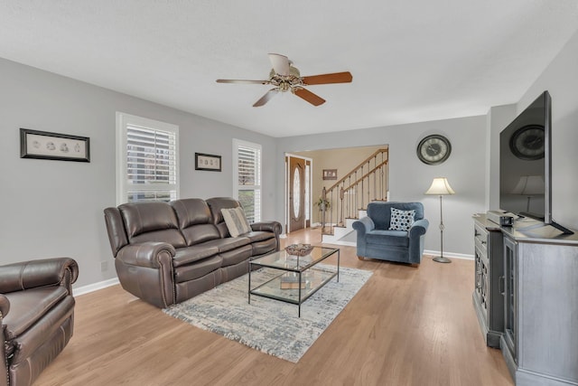 living area featuring stairs, ceiling fan, light wood-style flooring, and baseboards