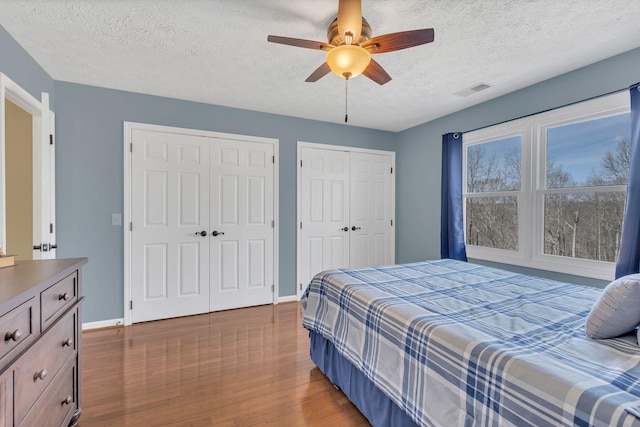 bedroom featuring ceiling fan, a textured ceiling, wood finished floors, baseboards, and multiple closets