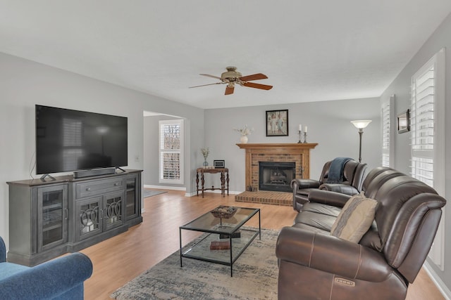 living area featuring light wood-type flooring, a fireplace, baseboards, and a ceiling fan