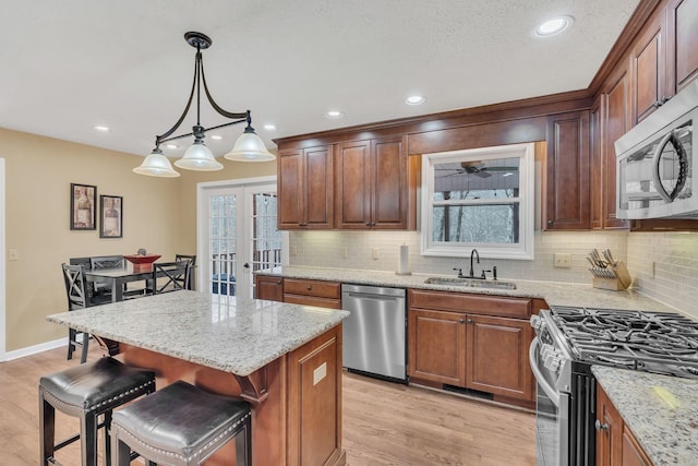 kitchen with a sink, appliances with stainless steel finishes, light stone countertops, a kitchen bar, and decorative light fixtures