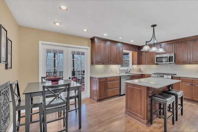 kitchen featuring light wood-style flooring, stainless steel appliances, a center island, light stone countertops, and pendant lighting