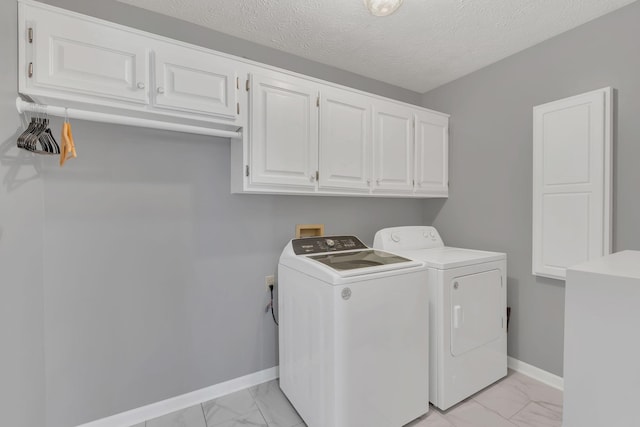 clothes washing area featuring a textured ceiling, washing machine and dryer, baseboards, marble finish floor, and cabinet space