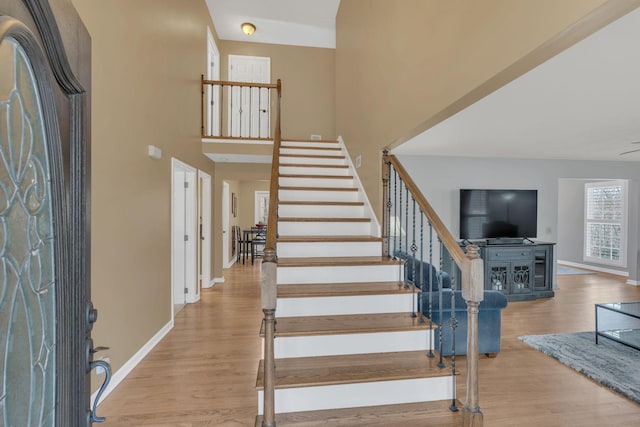 entryway with baseboards, stairway, a towering ceiling, and light wood-style floors