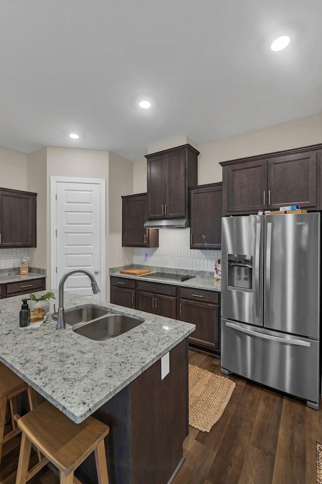 kitchen featuring under cabinet range hood, a breakfast bar, a sink, an island with sink, and stainless steel fridge