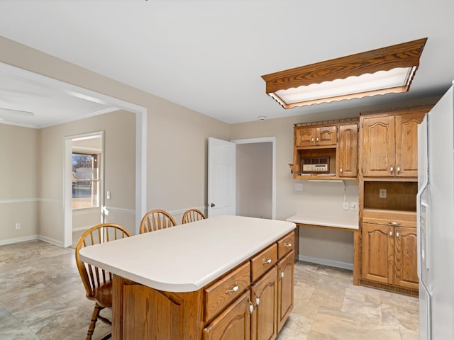 kitchen featuring baseboards, brown cabinets, a breakfast bar, a center island, and light countertops