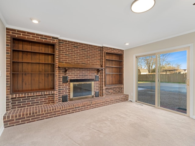 unfurnished living room featuring built in shelves, crown molding, a fireplace, and carpet floors