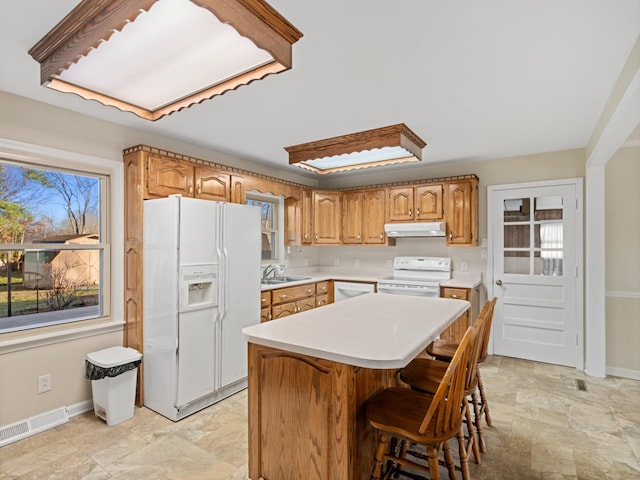 kitchen with under cabinet range hood, white appliances, visible vents, light countertops, and a center island