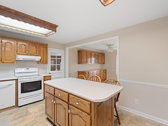 kitchen with under cabinet range hood, white appliances, baseboards, light countertops, and a center island