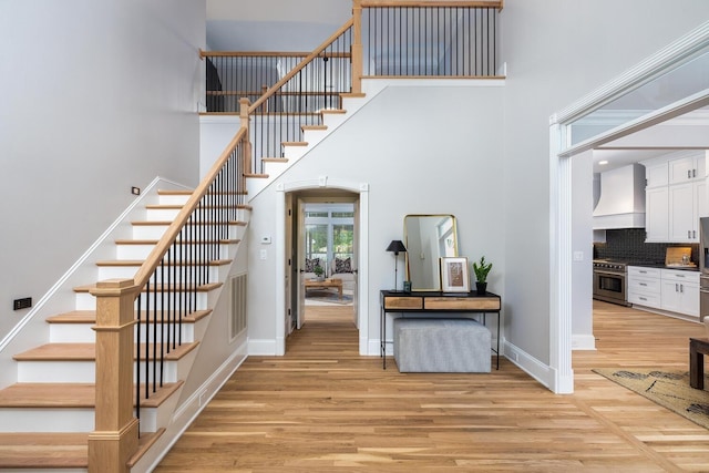 stairs featuring visible vents, a towering ceiling, baseboards, and wood finished floors