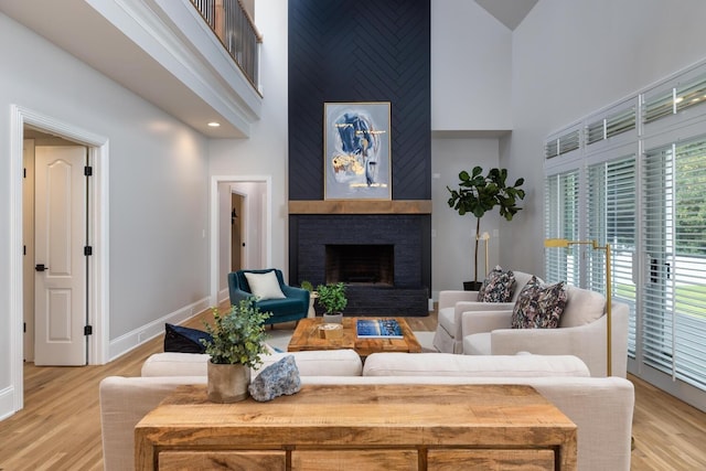 living room featuring light wood-style floors, a brick fireplace, baseboards, and a high ceiling