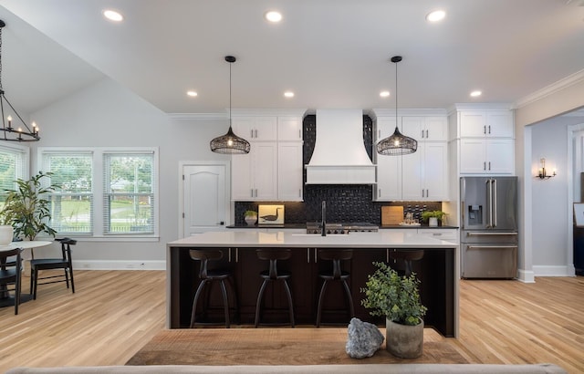 kitchen with light countertops, high end fridge, premium range hood, and an island with sink