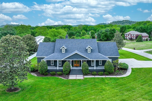 view of front of property featuring a front lawn, roof with shingles, and a wooded view