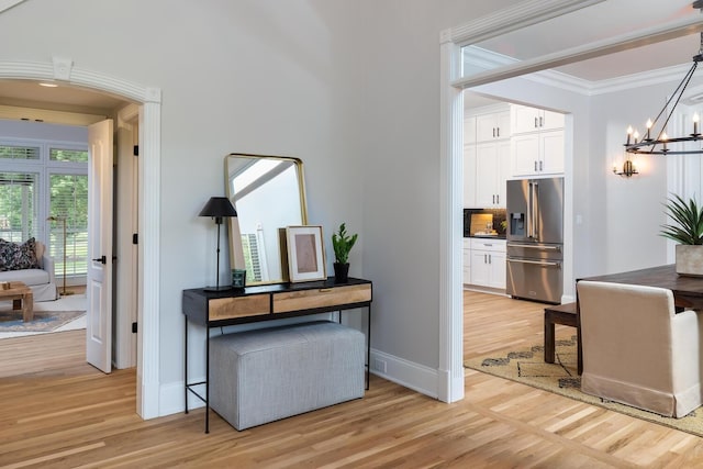 hall featuring light wood-style floors, ornamental molding, baseboards, and an inviting chandelier