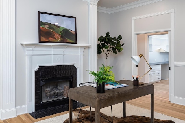 home office with light wood-type flooring, ornamental molding, a tiled fireplace, and baseboards