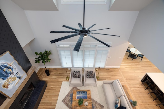 living area featuring ceiling fan, a towering ceiling, baseboards, and wood finished floors