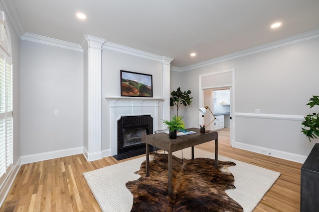 office space with a fireplace with flush hearth, baseboards, crown molding, and light wood finished floors