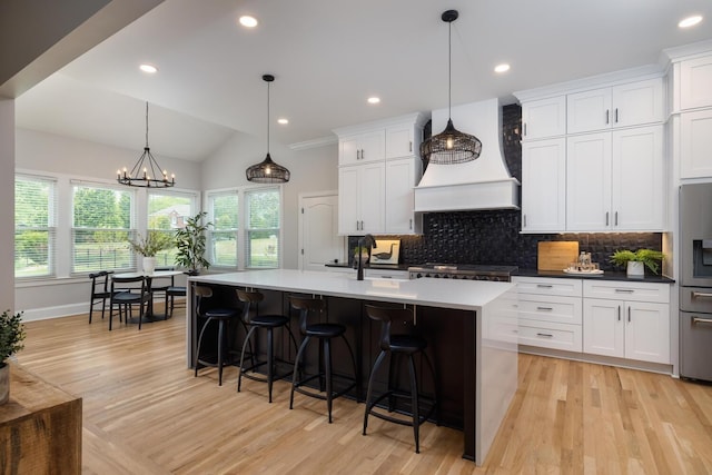 kitchen with white cabinets, a kitchen island with sink, custom range hood, and pendant lighting