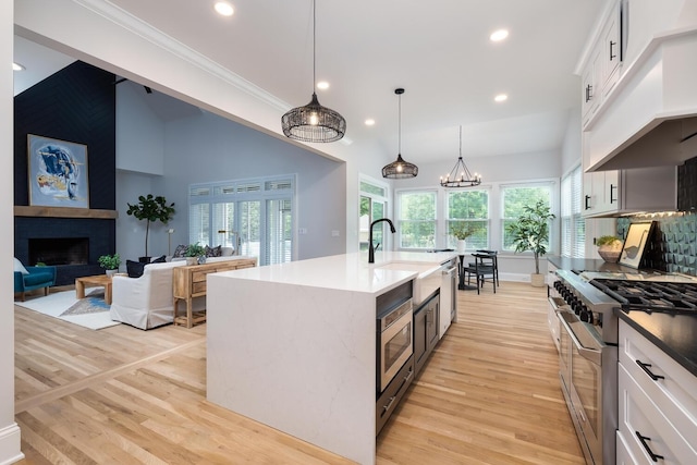 kitchen featuring a kitchen island with sink, white cabinets, light countertops, appliances with stainless steel finishes, and decorative light fixtures