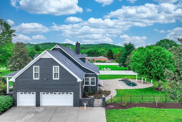 view of front of house with concrete driveway, a fenced front yard, a chimney, an attached garage, and a front lawn