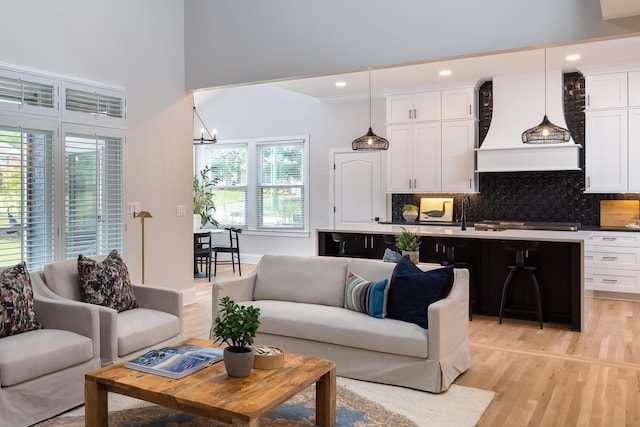 living area featuring baseboards, a high ceiling, light wood-type flooring, a notable chandelier, and recessed lighting