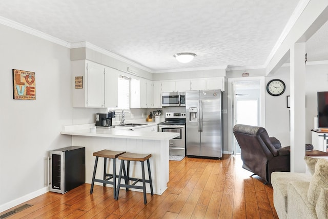 kitchen featuring stainless steel appliances, a peninsula, white cabinets, open floor plan, and light countertops