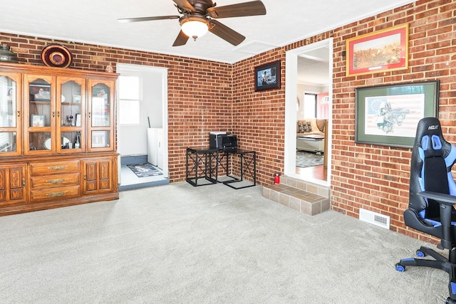 office featuring a ceiling fan, light colored carpet, visible vents, and brick wall