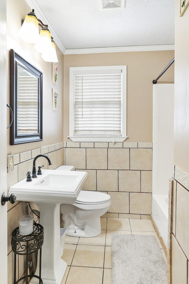 full bath with wainscoting, toilet, ornamental molding, tile patterned flooring, and tile walls