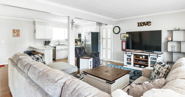 living area with baseboards, a textured ceiling, light wood-style flooring, and crown molding
