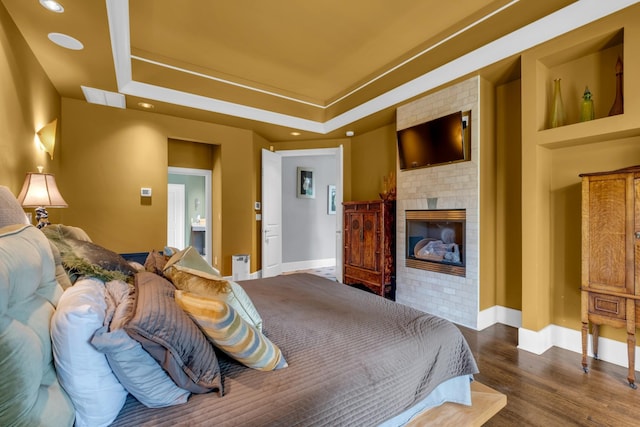 bedroom with a tray ceiling, visible vents, a brick fireplace, wood finished floors, and baseboards